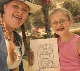 Cowgirl caricature artist with a young guest holding her Wanted caricature